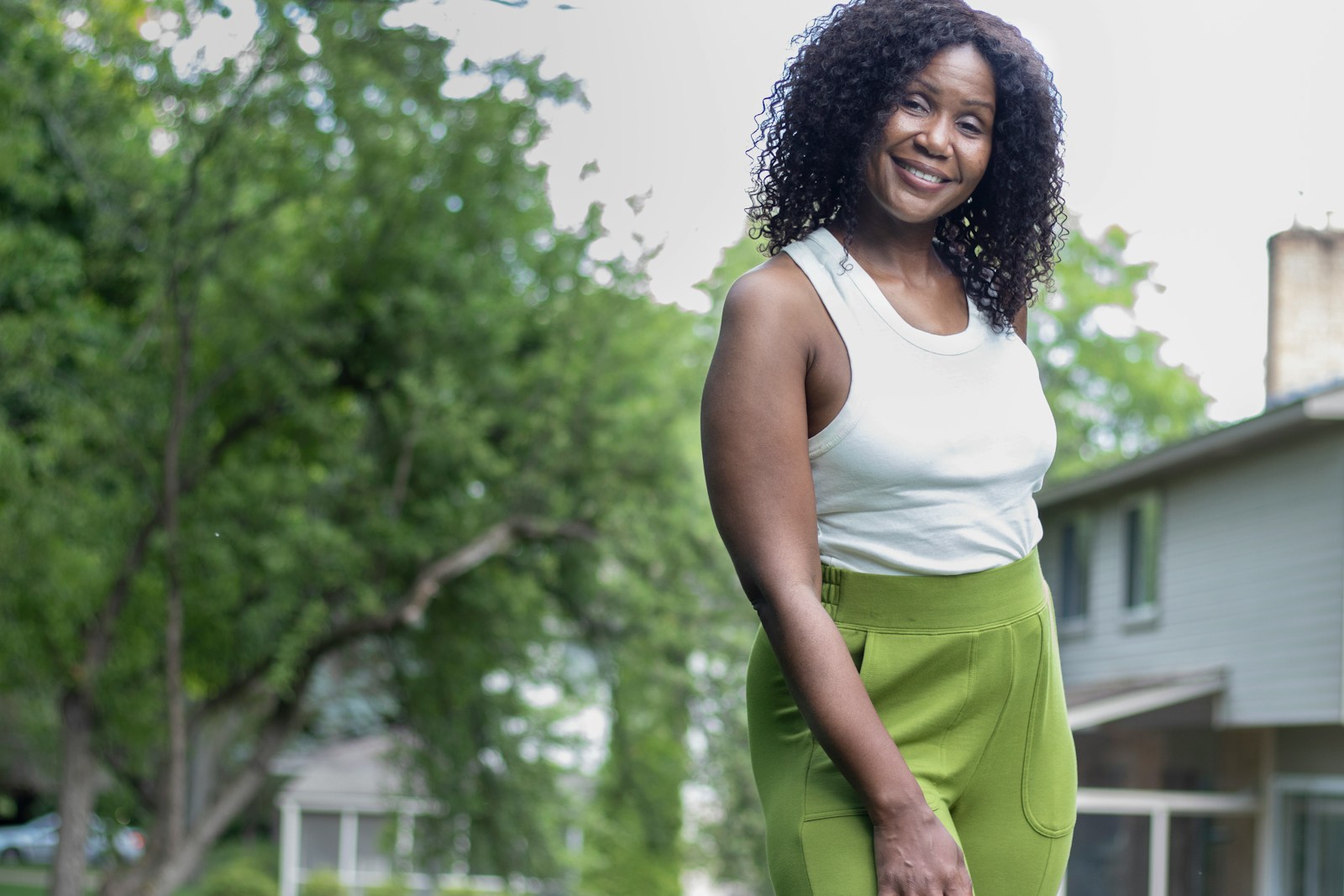 woman in white tank top and green shorts standing near green trees during daytime